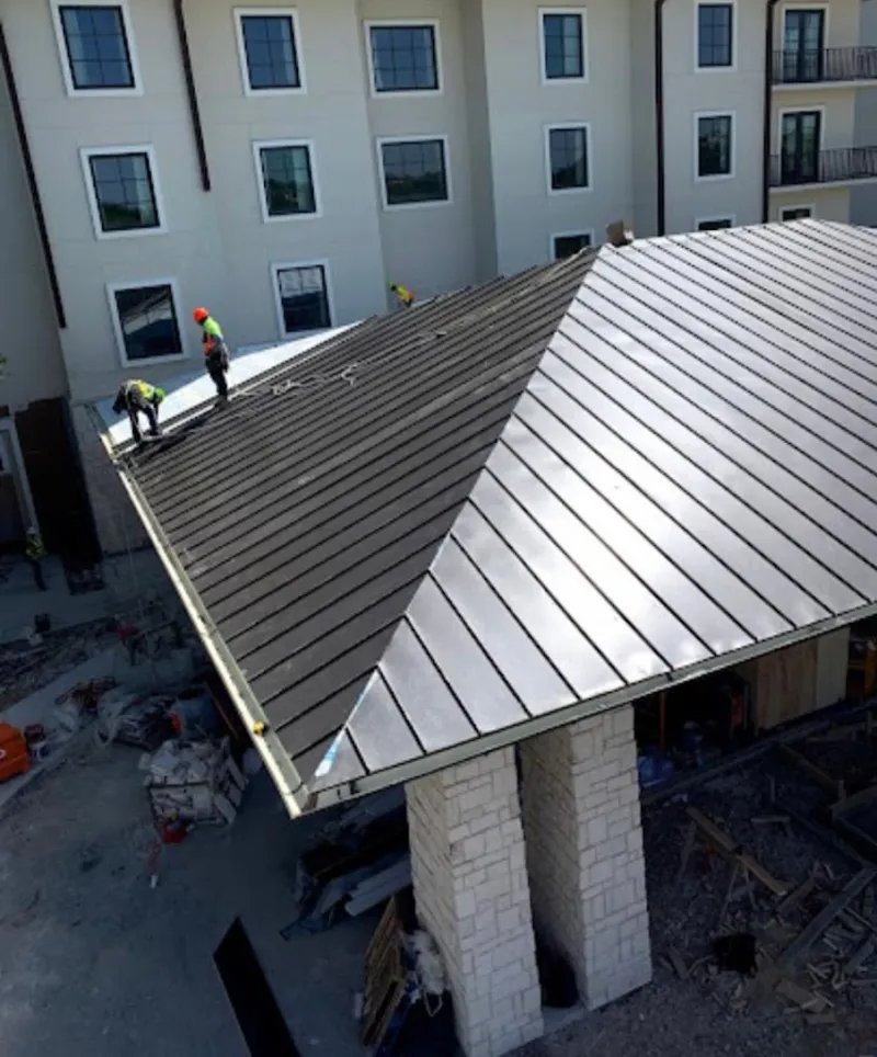 Crew installing standing seam metal roof panels on a commercial project in Buda